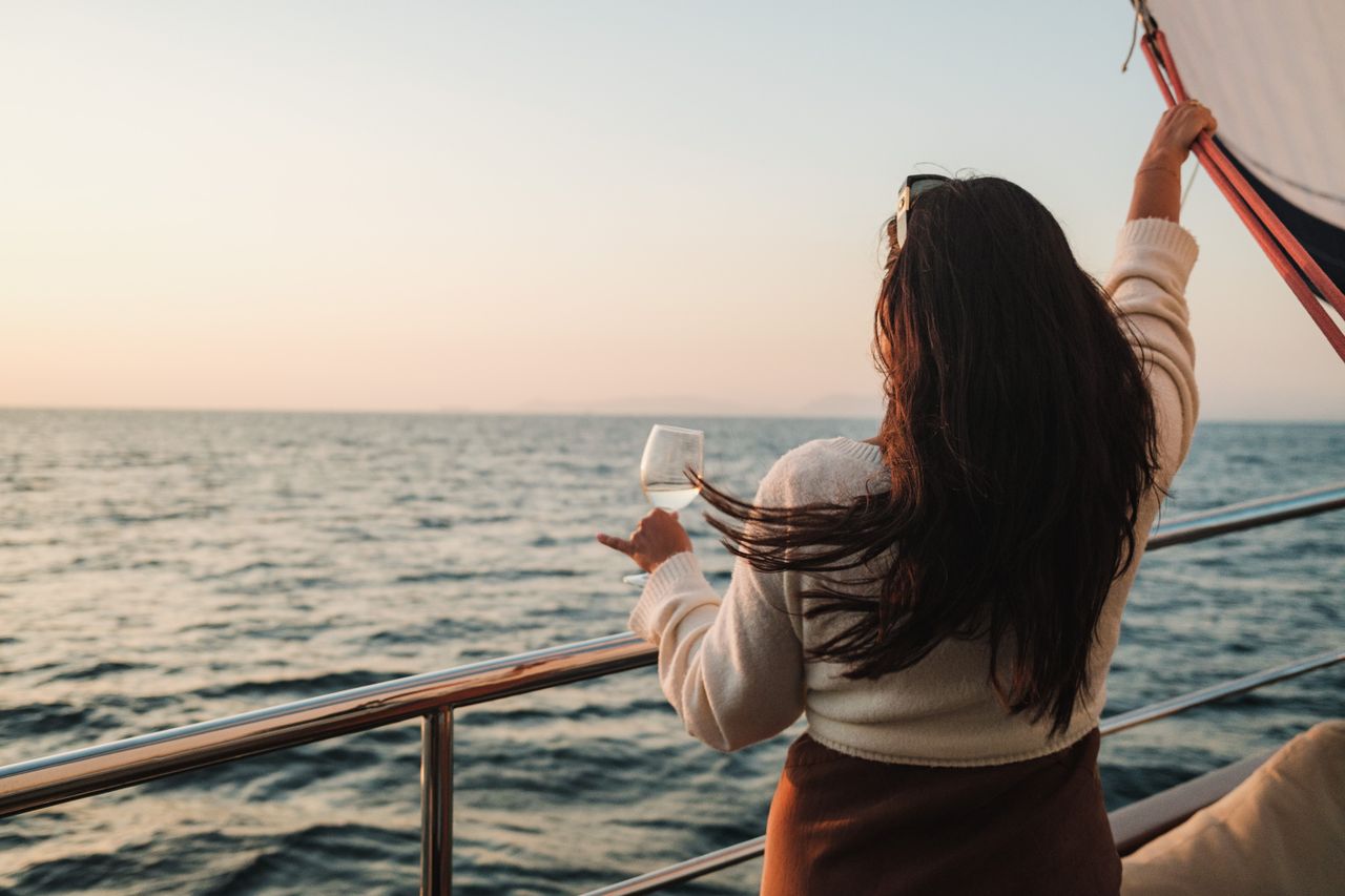 The Art of Drawing Readers In: Your attractive post title goes here A woman with long brunette hair enjoys a drink while sailing at sunset.